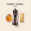 A perfume bottle labeled 'Golden Amber N118' on a light cream background, shown with a faceted amber crystal and a gold rectangular cap or packaging piece beside it. The bottle is clear glass with a dark metallic cap and a black central panel featuring a white snake-like logo.
