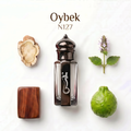 A perfume bottle labeled 'Oybek N127' centered on a white background, surrounded by botanical and wood props: a dried flower slice, a small purple flower sprig, a green pomelo, and a rectangular brown wood block.